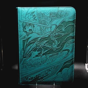 May include: A rectangular teal binder featuring an embossed manga-style illustration of a character and a dragon-like creature flying over a city. The text "ZWOOSH!" and "VAULTX" are visible on the front cover, which has a textured surface finish.