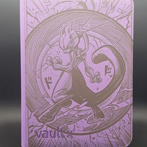 May include: A light purple card binder featuring a dark brown embossed illustration of the character Mewtwo in a dynamic pose. The design includes circular line patterns and Japanese katakana characters. The brand name vaultx is printed in purple.