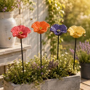 May include: Four ceramic flower garden stakes in red, orange, purple, and yellow, each featuring a textured, ruffled petal design with a yellow center. The flowers are mounted on thin black metal rods and are displayed in a rectangular planter.
