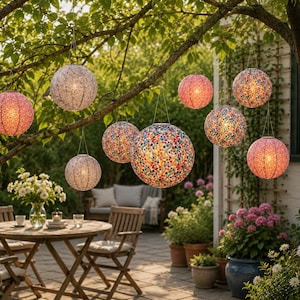 Könnte beinhalten: Eine Sammlung kugelförmiger Hängelaternen mit bunten Blumenmustern, die an Baumzweigen hängen. Jede Laterne enthält eine leuchtende Lichtquelle, die eine warme Beleuchtung auf der Außenterrasse erzeugt.
