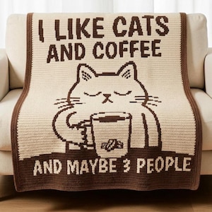 May include: A cream-colored crochet blanket with a dark brown border featuring a graphic of a cat holding a coffee mug. The text reads I LIKE CATS AND COFFEE AND MAYBE 3 PEOPLE. The design is rendered in a pixelated style with dark brown yarn.