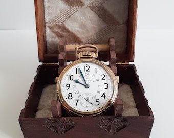 Puede incluir: Un reloj de bolsillo de oro con números romanos en la esfera, colocado dentro de una caja de madera con tallas intrincadas.