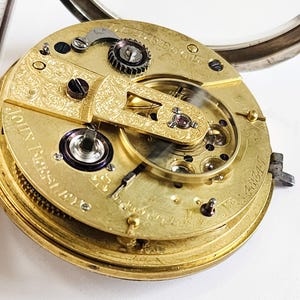 Könnte beinhalten: Nahaufnahme eines goldenen Taschenuhrwerks mit filigranen Gravuren und dem Text "John  T.  Berry  &  Co.  Liverpool  No.  48941".