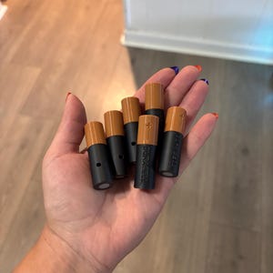 Pode incluir: Um conjunto de cinco pilhas cilíndricas Duracell, cada uma com uma base preta distinta e um topo de cor cobre. As pilhas estão dispostas em grupo, com a marca Duracell claramente gravada na lateral da unidade central.