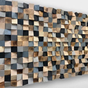 May include: A wall art piece composed of numerous small, square wooden blocks arranged in a grid. The blocks feature varying depths and a color palette of natural wood grain, light gray, dark gray, and solid black, creating a textured surface.