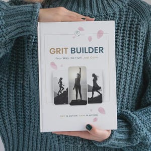 May include: A white book titled GRIT BUILDER with the subtitle Your Way. No Fluff. Just Calm. The cover features three black and white photographs of silhouettes in outdoor settings, accented by scattered pink petal illustrations and the text GRIT IN ACTION. CALM IN MOTION.