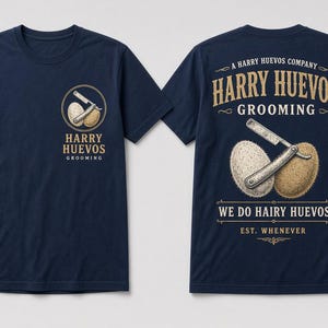 May include: A navy blue short-sleeve t-shirt featuring a graphic print on the front left chest and a larger version on the back. The design displays a straight razor resting on two textured eggs with the text Harry Huevos Grooming and We Do Hairy Huevos.