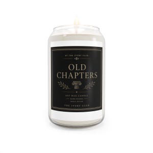 Puede incluir: Una vela de cera de soja de color blanco roto en un tarro de cristal transparente con una mecha encendida. La etiqueta negra tiene texto dorado que dice Old Chapters, By The Ivory Club, Soy Wax Candle, Hand Poured, Small Batch.