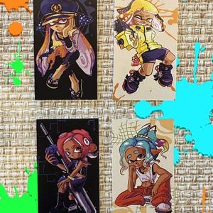May include: Four rectangular art prints featuring stylized cartoon characters from the Splatoon video game series. Each print displays a unique character in a dynamic pose, rendered with vibrant colors and distinct outfits against black or cream backgrounds.