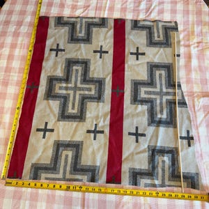 May include: A rectangular woven fabric piece featuring a beige background with dark gray geometric cross patterns and vertical red stripes. A yellow measuring tape shows a length of approximately 28 inches and a width of 27 inches.