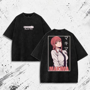 May include: A black acid-wash t-shirt featuring the Chainsaw Man logo on the front chest. The back displays a graphic of the character Makima with pink hair, wearing a white shirt and black tie, accompanied by Japanese text and the name Makima.