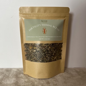 May include: A brown kraft paper pouch containing a herbal tea blend. The label features the text Soul of the Earth, FERTILITY HERBAL BLEND, A BOTANICAL TEA CRAFTED FOR SEASONS OF CREATION, and NET WT. 1.7 oz. (50g) with a small orange figure icon.