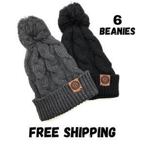 May include: Six gray and black cable knit beanies with pom poms and a leather patch. The patch has a logo and two silver studs.  "6 Beanies" is written in black text on a white background.