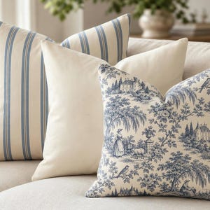 Close-up of the layered pillow set: solid ivory, slate blue toile de Jouy and blue ticking stripe covers