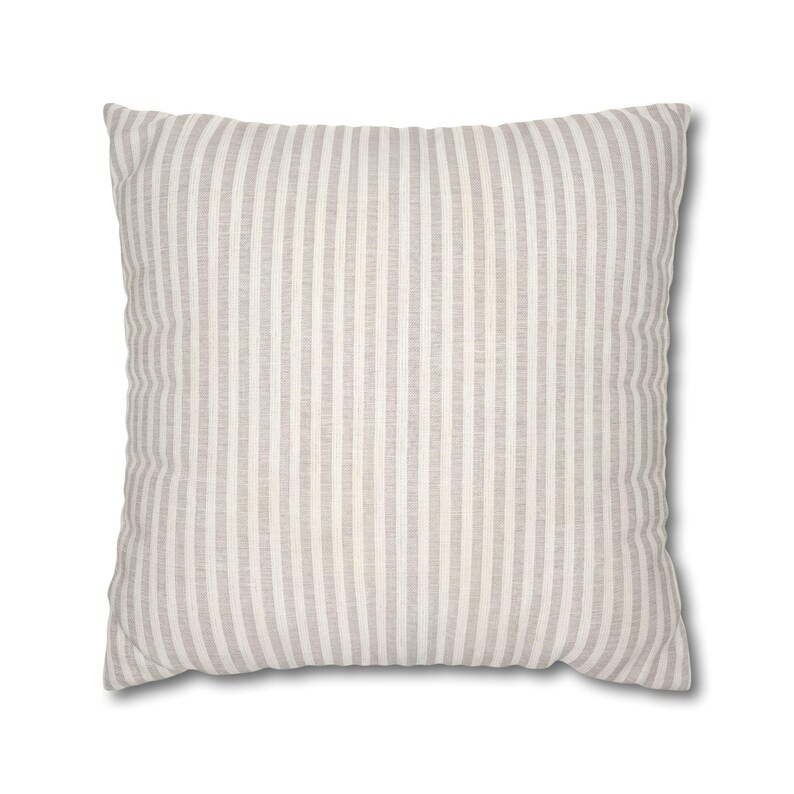 A square beige pillow with fine white vertical stripes on a plain white background.