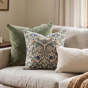 A light beige sofa is styled with a dark green velvet pillow, a botanical print accent pillow, and a textured cream lumbar pillow.