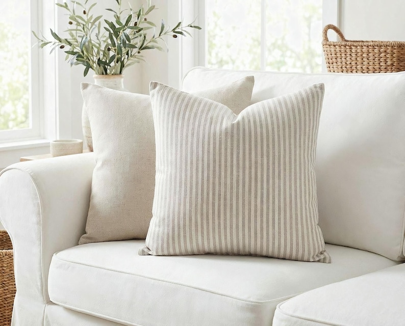 Taupe and cream ticking stripe pillow cover on a white slipcovered sofa in a bright farmhouse living room
