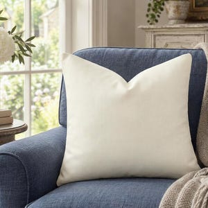 Solid warm ivory pillow cover on a slate blue armchair beside a window