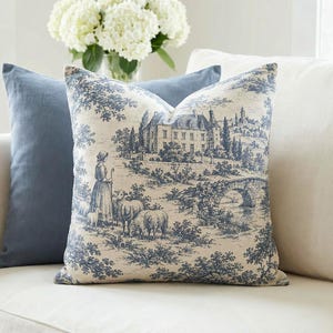 Slate blue pastoral toile de Jouy pillow cover with chateau and sheep on a cream sofa with a slate blue pillow