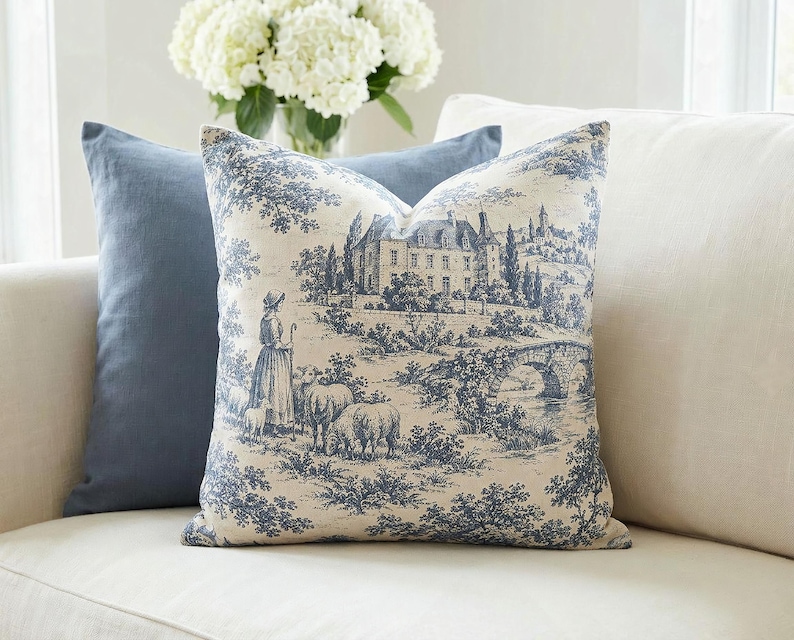 Slate blue pastoral toile de Jouy pillow cover with chateau and sheep on a cream sofa with a slate blue pillow