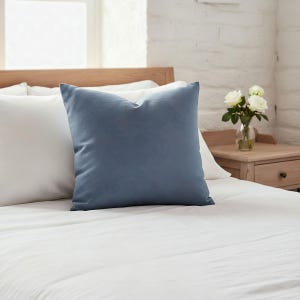 Solid slate blue pillow on a white linen bed in a French country bedroom