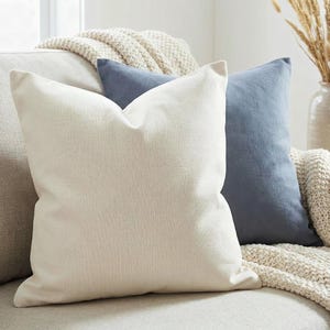 Solid ivory pillow cover on an oatmeal sofa with a slate blue pillow and chunky knit throw