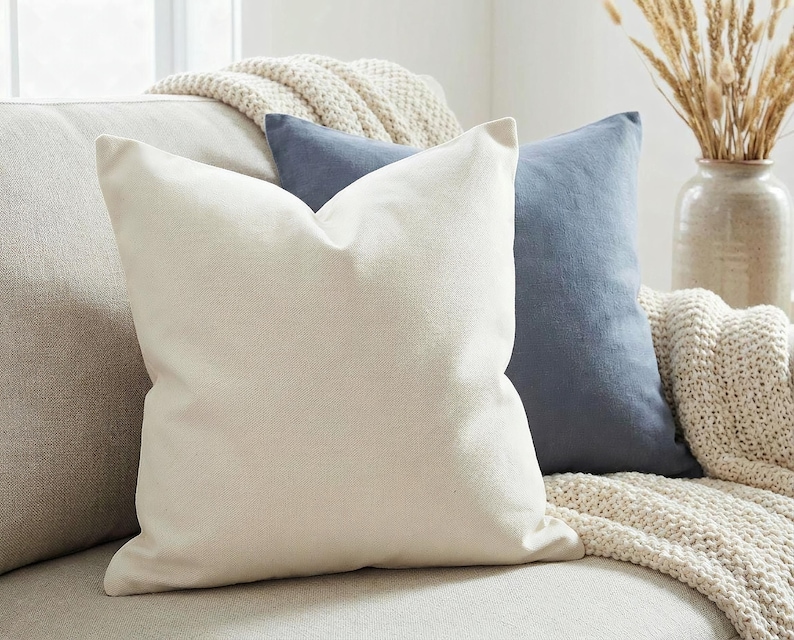 Solid ivory pillow cover on an oatmeal sofa with a slate blue pillow and chunky knit throw