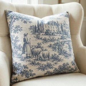 Close-up of the slate blue pastoral toile de Jouy pillow cover with shepherdess, sheep and chateau in a cream wingback chair
