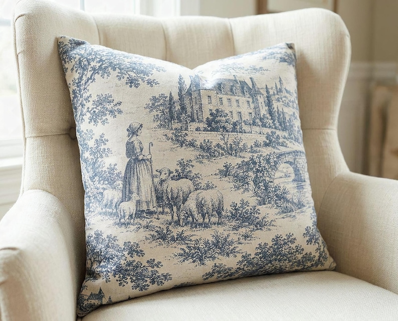 Close-up of the slate blue pastoral toile de Jouy pillow cover with shepherdess, sheep and chateau in a cream wingback chair