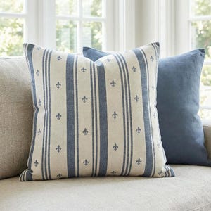 Slate blue fleur de lis ticking stripe pillow cover on an oatmeal linen sofa with a slate blue pillow