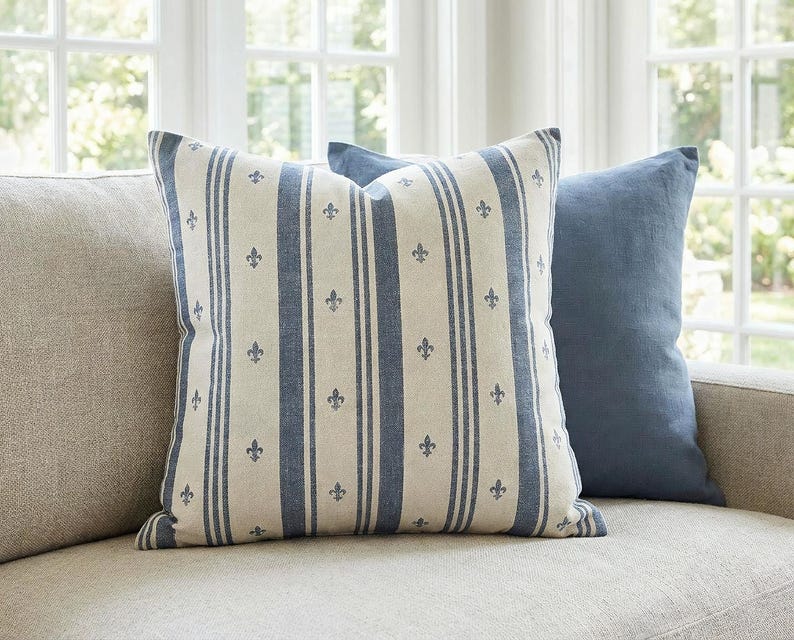 Slate blue fleur de lis ticking stripe pillow cover on an oatmeal linen sofa with a slate blue pillow