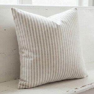 Close-up of the taupe and cream ticking stripe pillow cover on a white farmhouse bench