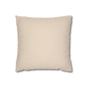 May include: A square throw pillow with a solid, plain light beige fabric cover. The pillow has a simple, uniform design with smooth edges and a consistent, neutral color throughout the entire surface of the square-shaped cushion.