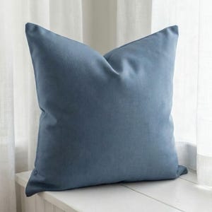 Close-up of the solid slate blue pillow cover on a window seat with sheer curtains, soft printed linen-look finish
