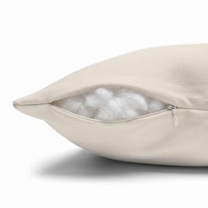 A close-up view of an ivory pillow cover partially unzipped, revealing fluffy white stuffing inside.