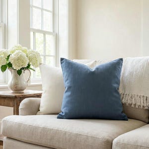 Solid slate blue linen-look pillow cover on an oatmeal linen sofa with an ivory pillow and white hydrangeas