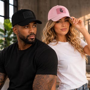May include: A black baseball cap and a light pink baseball cap, both featuring a rectangular patch on the front with a crown icon and the letters HW. The caps have a curved brim and a structured crown, providing a classic athletic headwear style.