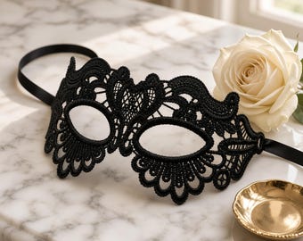 May include: A black lace masquerade mask featuring intricate floral and scrollwork patterns with two oval eye openings. The mask is constructed from detailed embroidery and includes thin black satin ribbons attached to the sides for securing.
