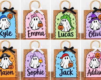 May include: Eight brown paper gift bags with handles, each featuring a scalloped-edge rectangular label with a ghost illustration and a name. The ghosts wear various accessories like hats or bows and hold pumpkins or candy, topped with a small bow.