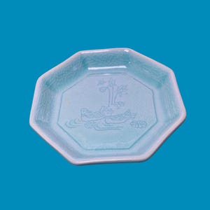 May include: An octagonal light blue ceramic dish featuring a crackle glaze finish. The center of the dish displays an embossed design of two ducks swimming in water with lotus flowers and leaves positioned above them in a simple line art style.