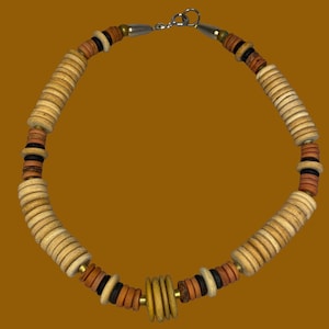 Puede incluir: Un collar con un patrón repetitivo de cuentas de madera circulares en tonos beige, marrón, negro y amarillo. Las cuentas están ensartadas en un cordón y aseguradas con un cierre de metal plateado en la parte superior, formando un círculo.