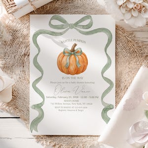 May include: A rectangular baby shower invitation card featuring a watercolor orange pumpkin with a sage green ribbon bow, framed by a sage green ribbon border. The text reads A LITTLE PUMPKIN IS ON THE WAY, Olivia Vance, Saturday, February 23, 2058, 12:00 - 5:00 PM, MAYA'S HOME, 742 Willow Avenue, New York, NY 10028, RSVP TO MAIVE AT 555-019-2838, Registry: Amazon & Target.