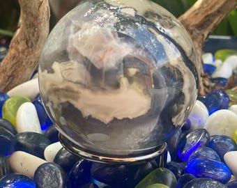 May include: A polished, black and white agate sphere on a silver stand. The sphere is surrounded by blue, green, and white stones.