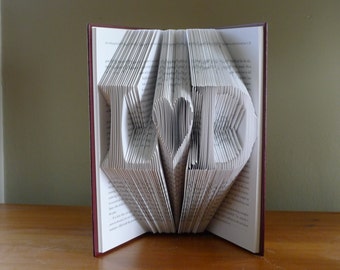 May include: A book with the word "LOVE" folded into the pages. The letters are made of folded pages and the "O" is shaped like a heart.