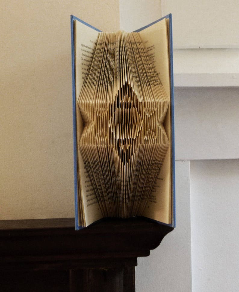May include: A book folded into a three-dimensional star shape. The book is open and the pages are folded to create a star design. The book is blue and has a white background.