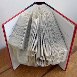 K&ouml;nnte beinhalten: Ein Buch, das zu einem Herz gefaltet ist. Das Buch hat einen roten und schwarzen Einband. Die Seiten sind gefaltet, um eine dreidimensionale Herzform zu erzeugen.