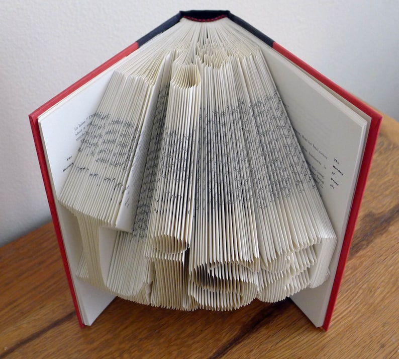 K&ouml;nnte beinhalten: Ein Buch, das zu einem Herz gefaltet ist. Das Buch hat einen roten und schwarzen Einband. Die Seiten sind gefaltet, um eine dreidimensionale Herzform zu erzeugen.