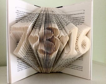 May include: A book with pages folded into the shape of the number 2016. The book is open and the pages are folded to create a three-dimensional effect.