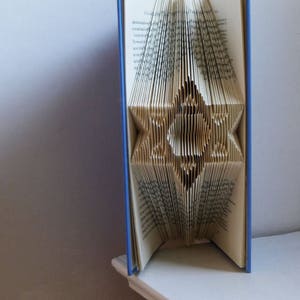 May include: A blue book with the pages folded into a star shape. The book is standing upright on a white surface.