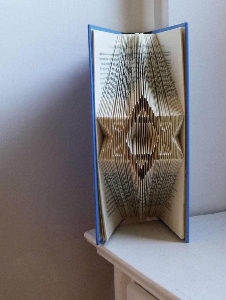May include: A blue book with the pages folded into a star shape. The book is standing upright on a white surface.
